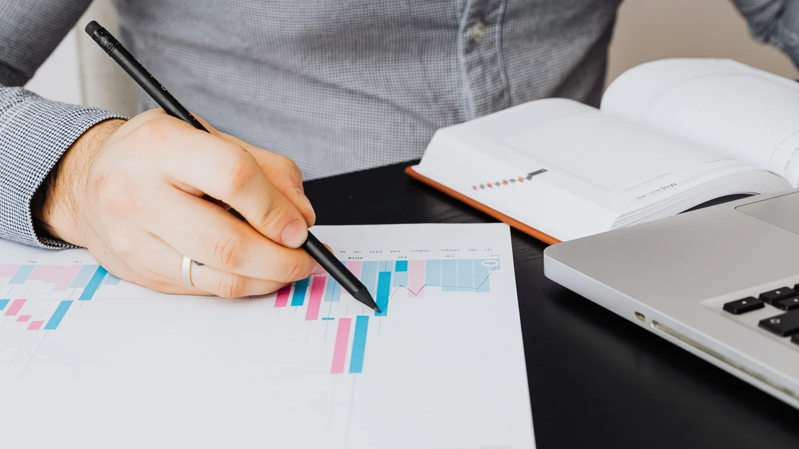 An analyst examining a printed graph beside a laptop and notebook