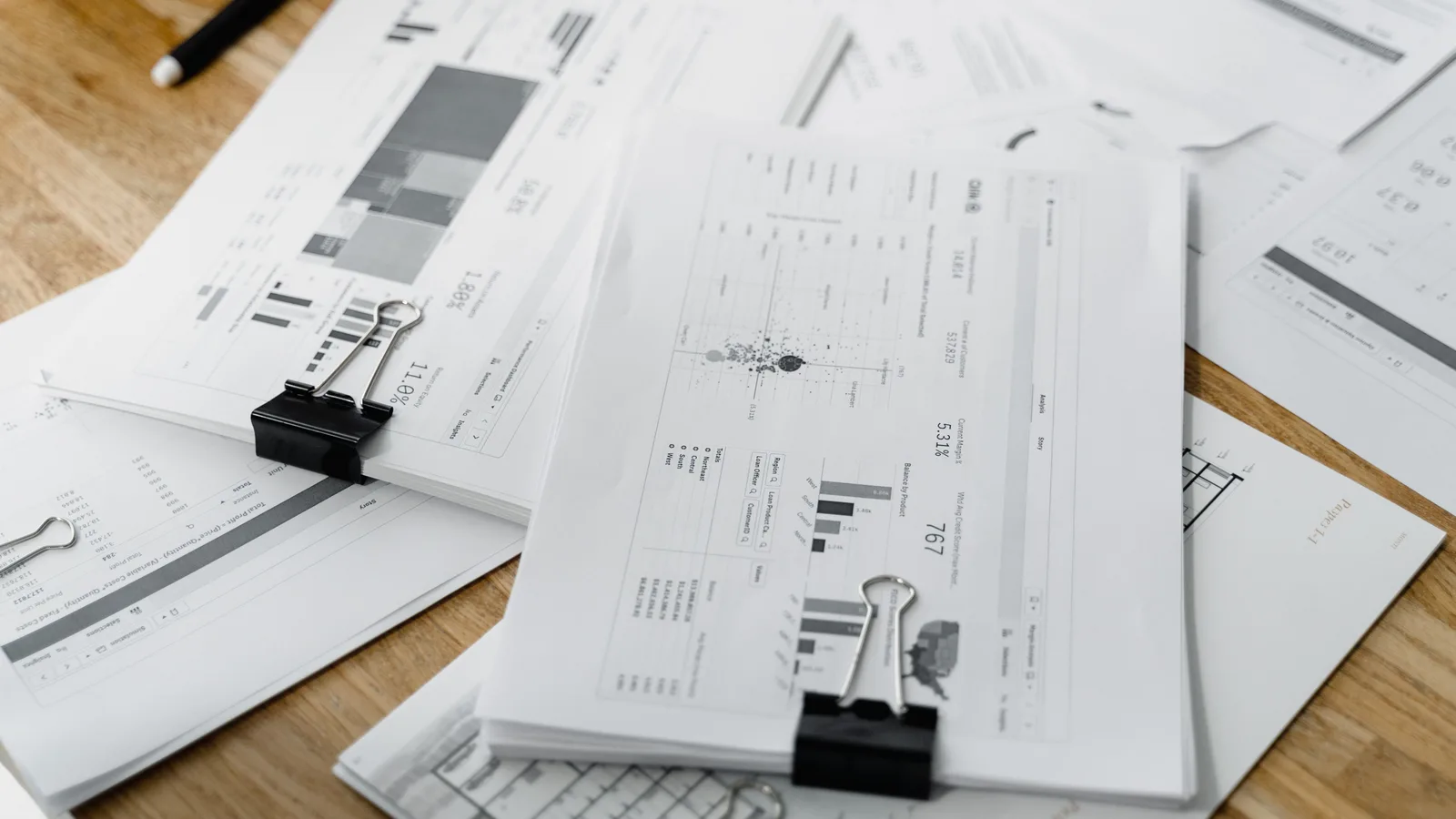 A stack of clipped financial reports and graphs on a wooden desk